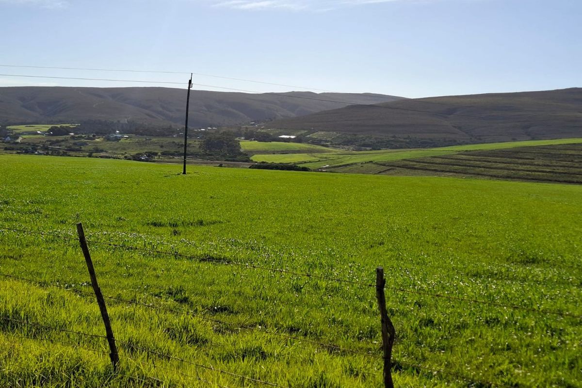 A scenic view of expansive green farmland with rolling hills in the background, featuring a wire fence and utility pole in the foreground.