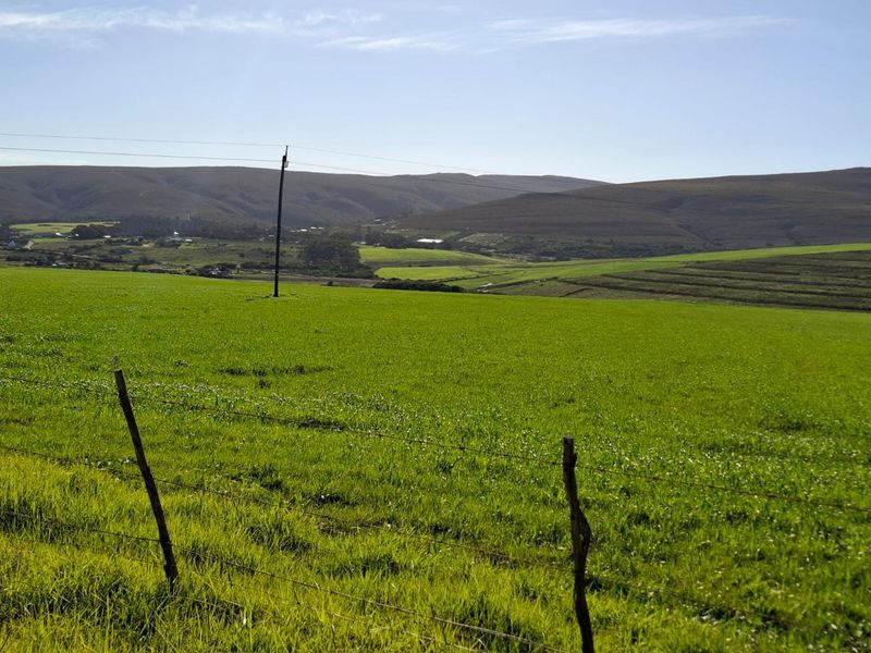 A scenic view of expansive green farmland with rolling hills in the background, featuring a wire fence and utility pole in the foreground.