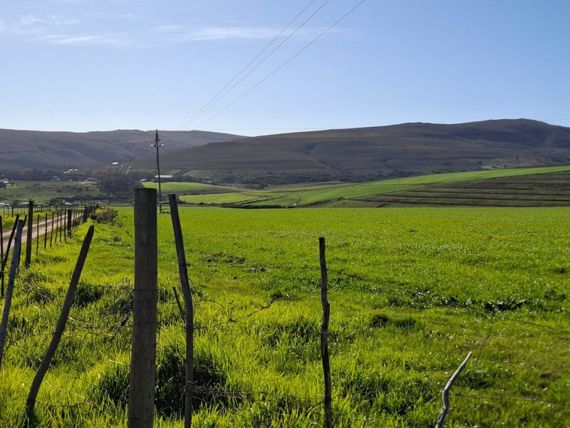 A scenic view of expansive green farm fields and rolling hills, framed by a traditional wire and wooden post fence.