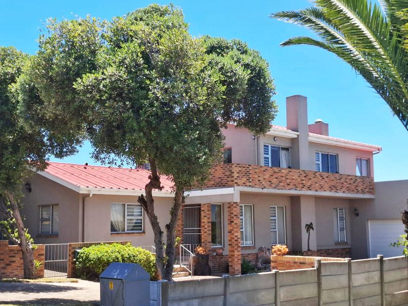 A two-story residential house featuring a red metal roof, brick detailing, a balcony, and a secure precast concrete boundary wall.