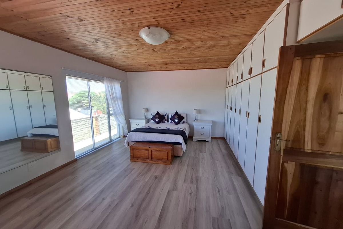 Spacious bedroom featuring extensive built-in cupboards, a warm timber-clad ceiling, modern laminate flooring, and large sliding doors providing natural light.