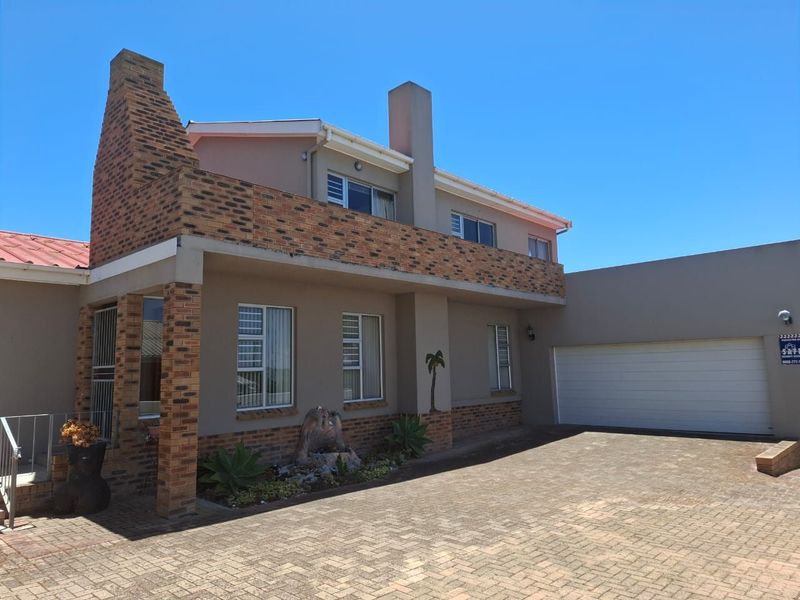 Front elevation of a two-story house featuring a brick chimney, balcony, paved driveway, and an integrated garage.
