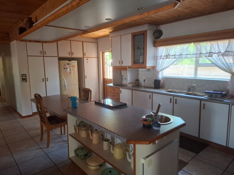 A functional kitchen featuring a central island, ample built-in cabinetry, double basin sink, and timber ceiling details, offering a traditional layout with potential for modernization.