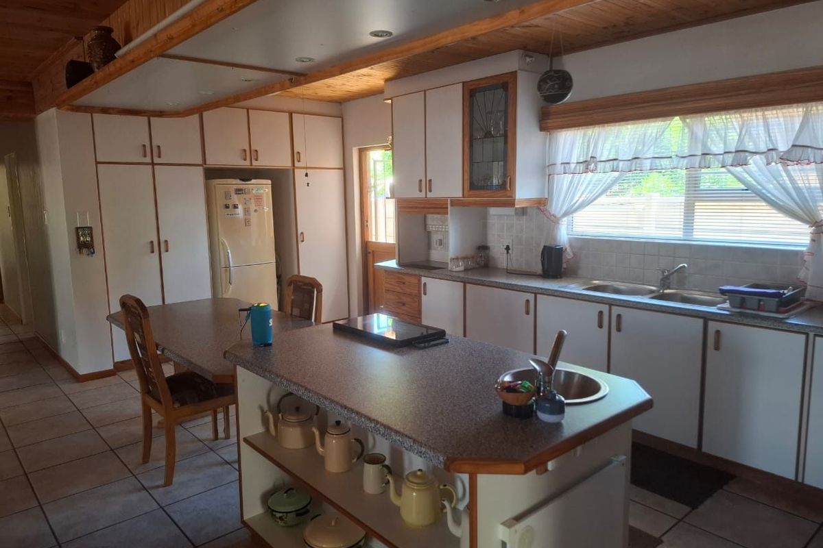 A functional kitchen featuring a central island, ample built-in cabinetry, double basin sink, and timber ceiling details, offering a traditional layout with potential for modernization.