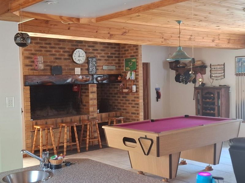 Spacious living area featuring a prominent built-in brick fireplace with timber mantel, exposed wood beam ceiling, and tiled flooring, ideal for entertainment.