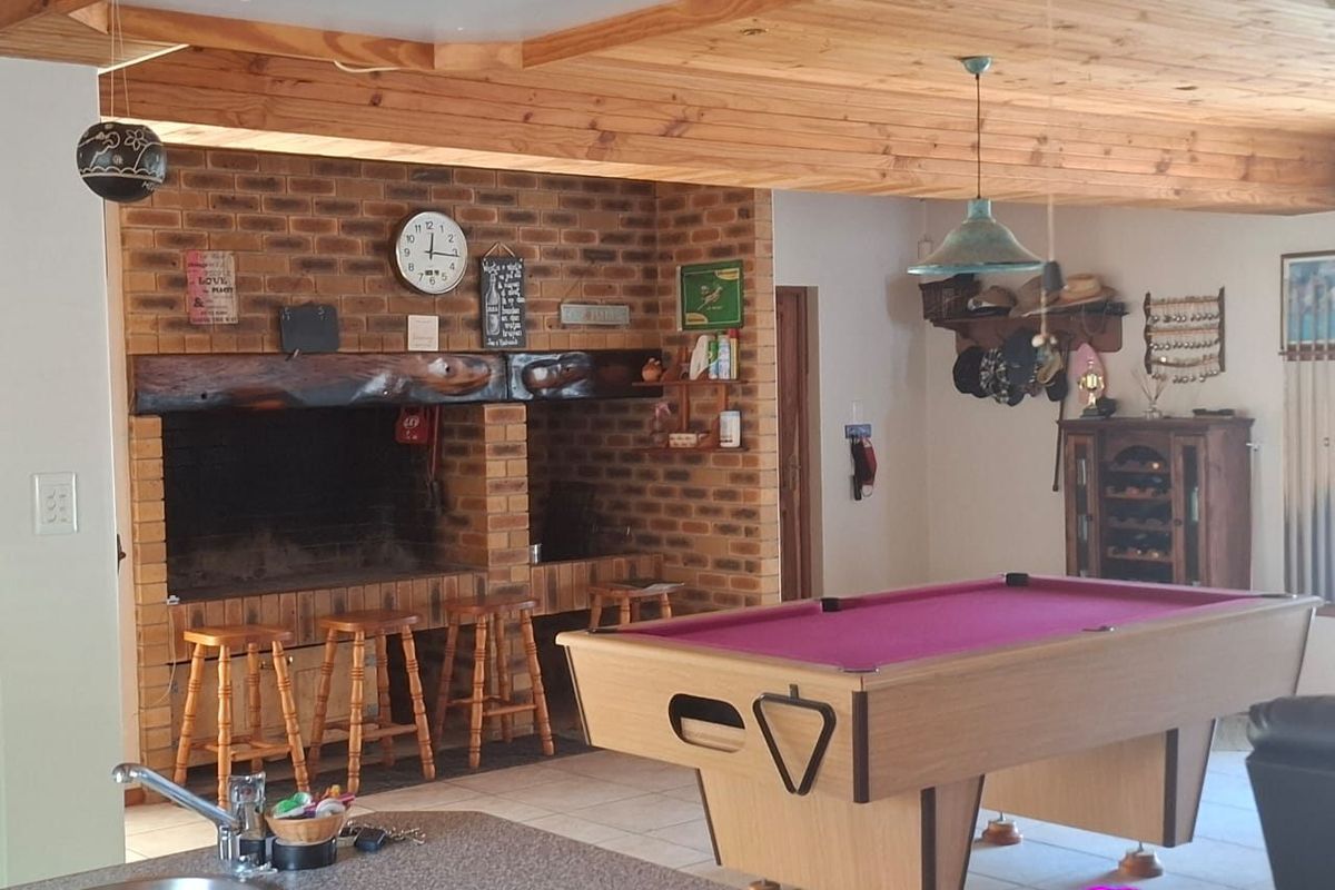 Spacious living area featuring a prominent built-in brick fireplace with timber mantel, exposed wood beam ceiling, and tiled flooring, ideal for entertainment.