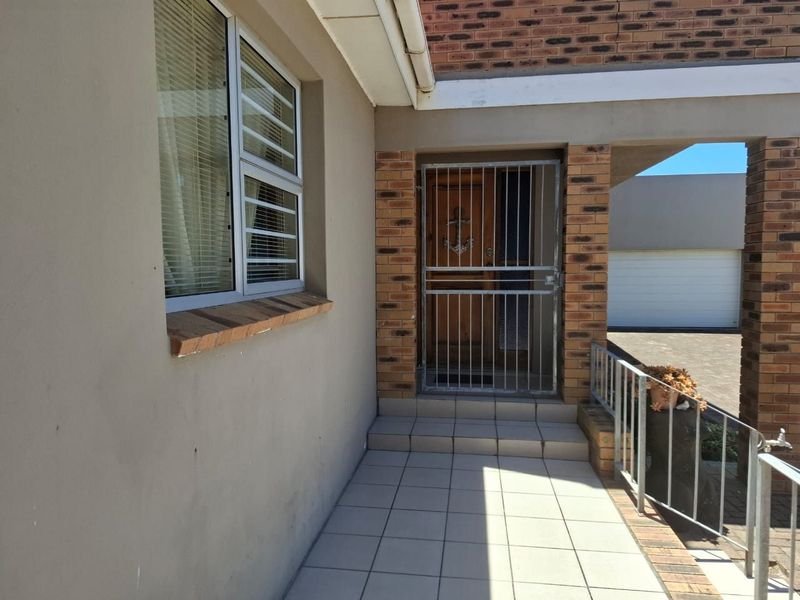 A covered entrance porch featuring tiled flooring, a security gate, and brick accents, providing a secure and functional entry point to the home.