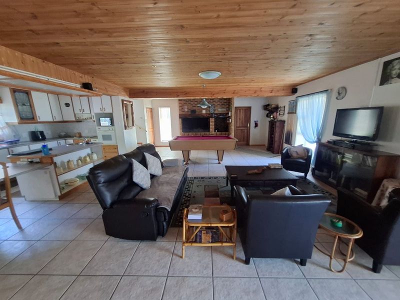 Spacious open-plan living area featuring a timber-clad ceiling, tiled floors, a brick fireplace, and an integrated kitchen with built-in cabinetry.