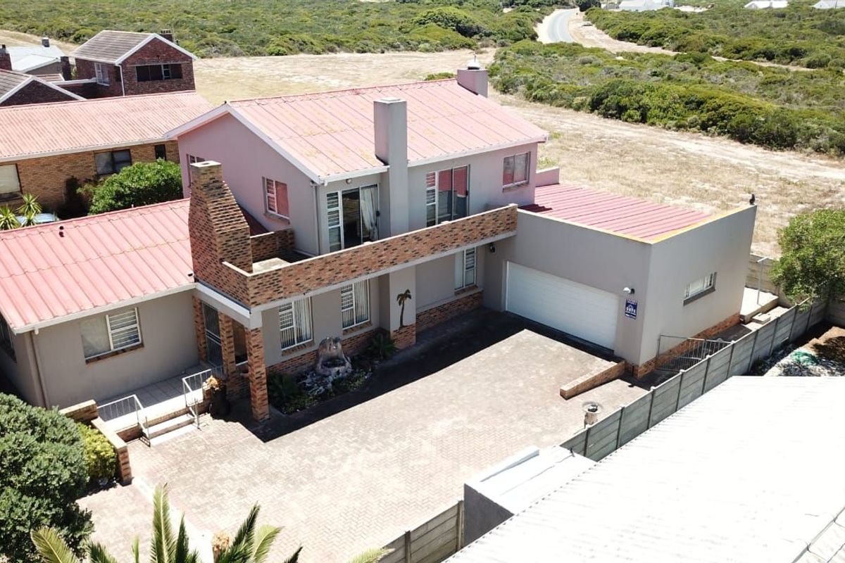 Aerial view of a two-story residential property featuring a paved driveway, double garage, and balcony, set within a coastal landscape.