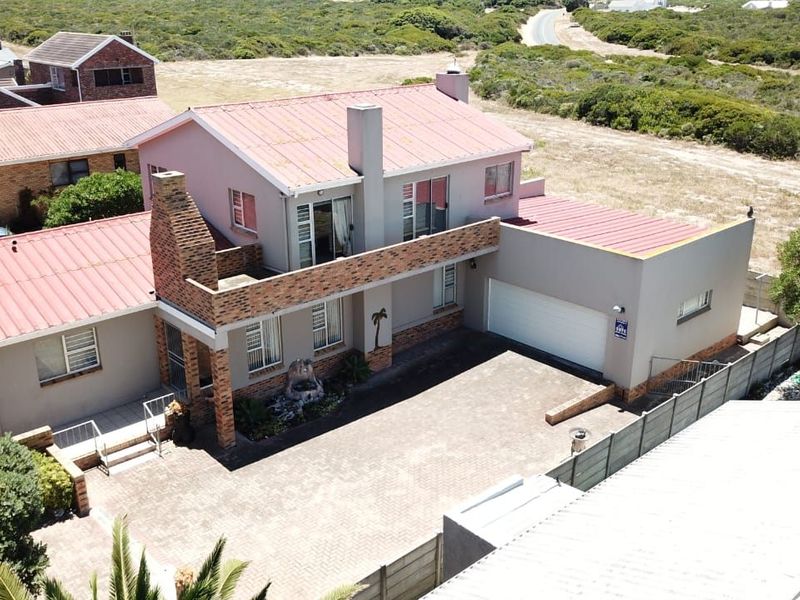 Aerial view of a two-story residential property featuring a paved driveway, double garage, and balcony, set within a coastal landscape.