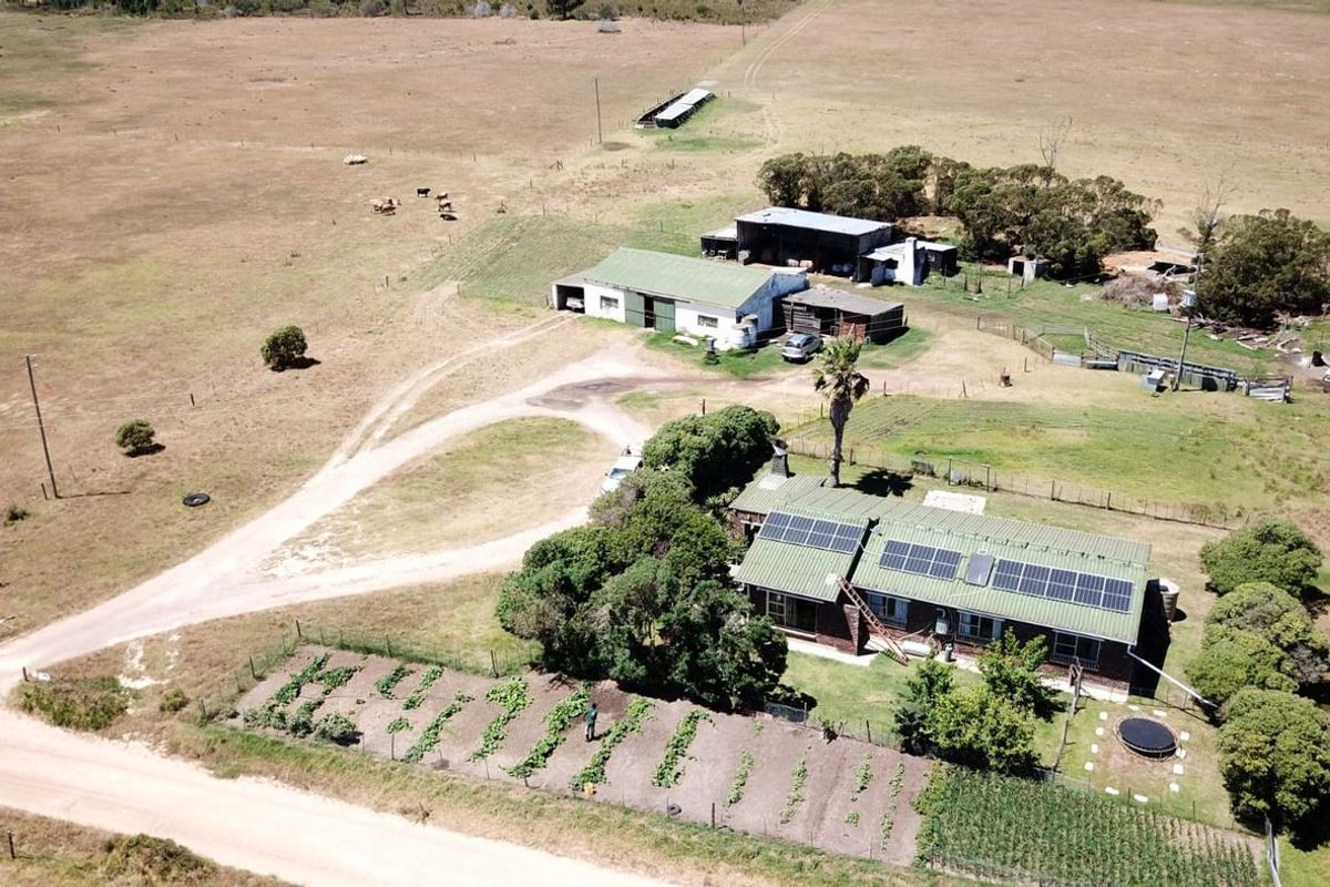 Aerial view of a farm property featuring a main residence with solar panels, surrounding outbuildings, a vegetable garden, and expansive open land.
