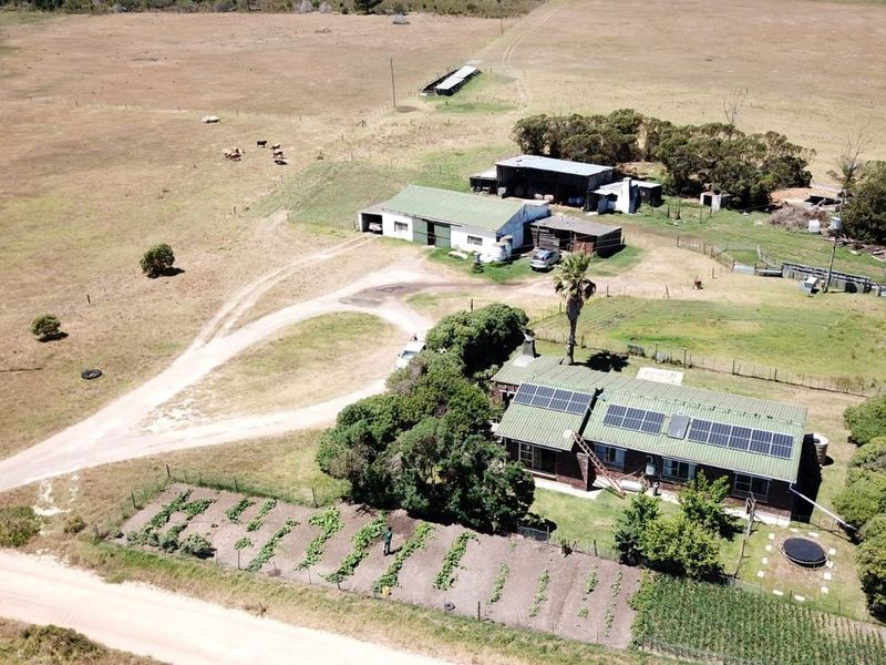Aerial view of a farm property featuring a main residence with solar panels, surrounding outbuildings, a vegetable garden, and expansive open land.