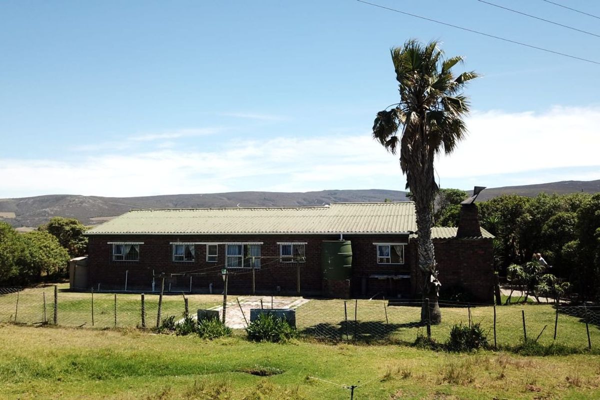 Rear view of a single-story brick farmhouse featuring a corrugated metal roof, external chimney, and an adjacent water tank set within a rural landscape.