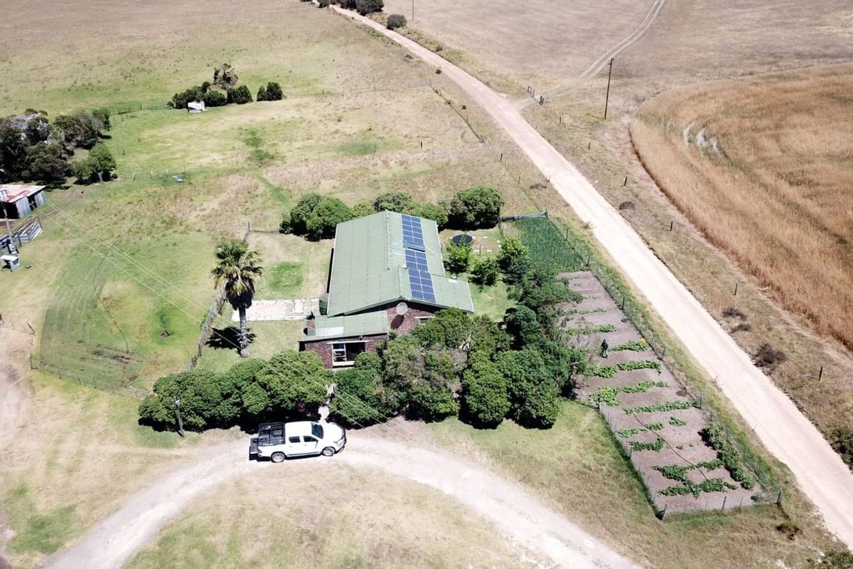 Aerial view of a farm property featuring a main residence with solar panels, a large garden, and surrounding agricultural land.