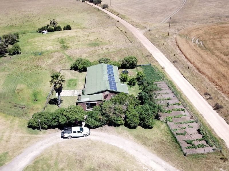 Aerial view of a farm property featuring a main residence with solar panels, a large garden, and surrounding agricultural land.