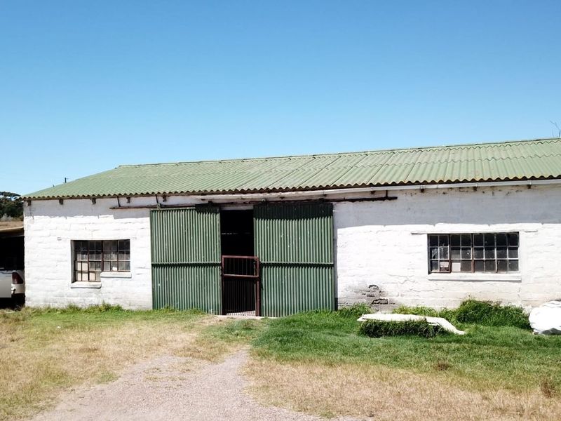 A rustic farm outbuilding featuring masonry walls, a corrugated metal roof, and large sliding barn doors, suitable for storage or agricultural use.
