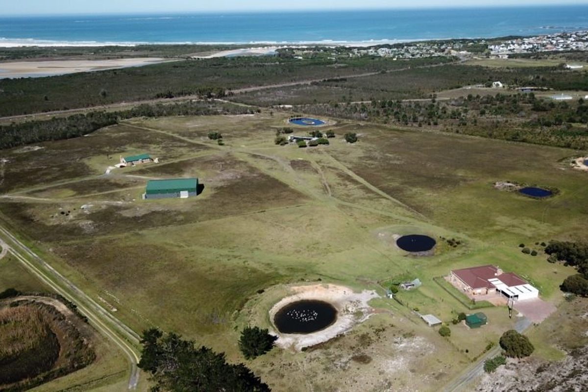 Aerial view of a large farm property featuring multiple outbuildings, several dams, and a main residence, set against a coastal landscape.