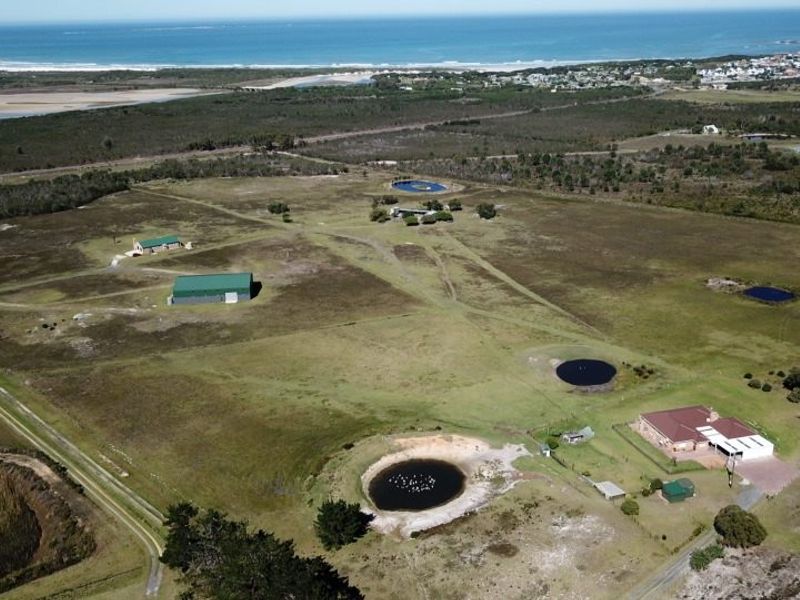 Aerial view of a large farm property featuring multiple outbuildings, several dams, and a main residence, set against a coastal landscape.