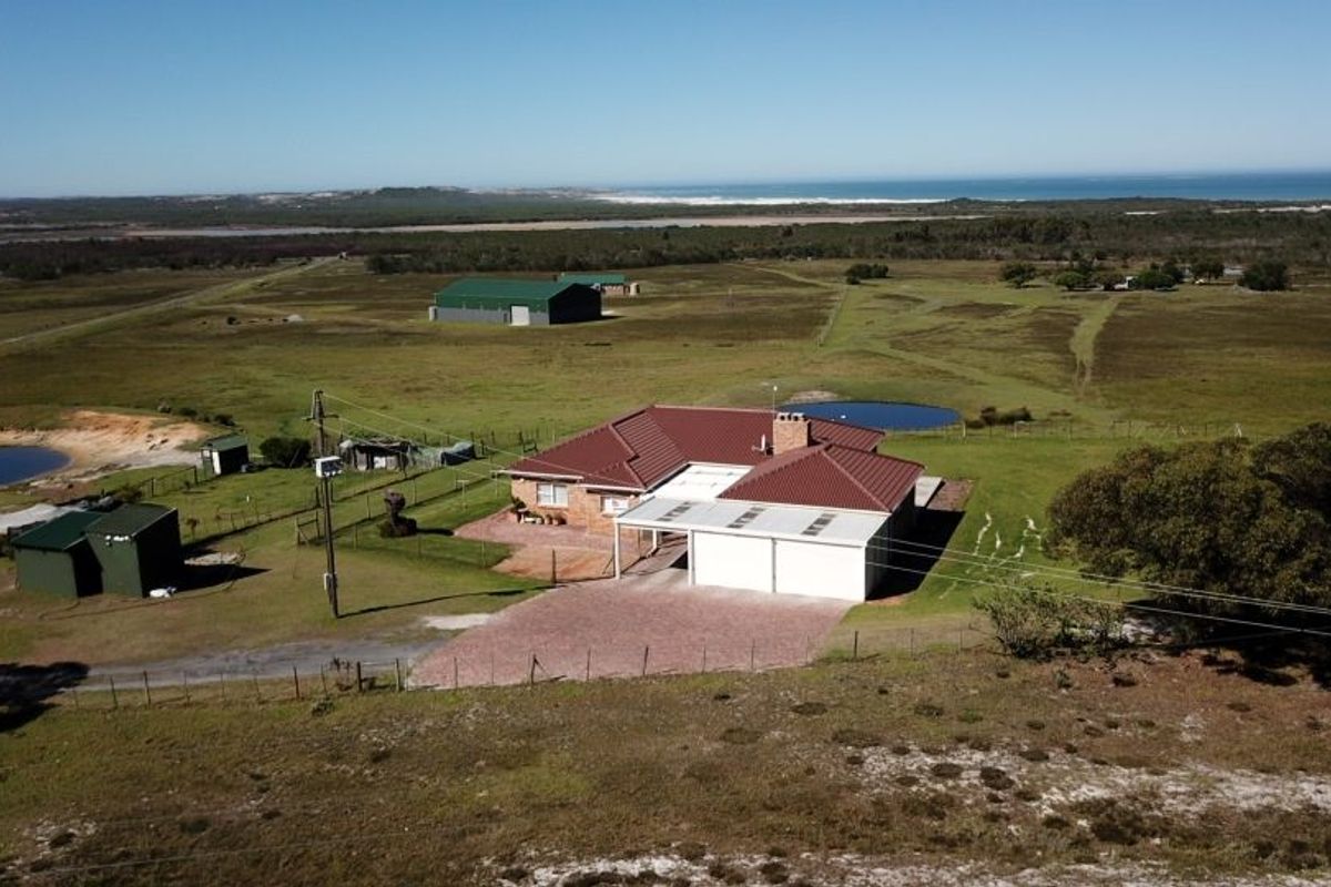 Aerial view of a farm property featuring a main residence with a metal roof, double garage, outbuildings, and surrounding rural landscape with water features.