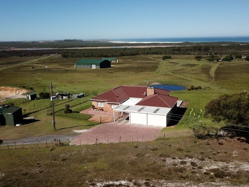 Aerial view of a farm property featuring a main residence with a metal roof, double garage, outbuildings, and surrounding rural landscape with water features.