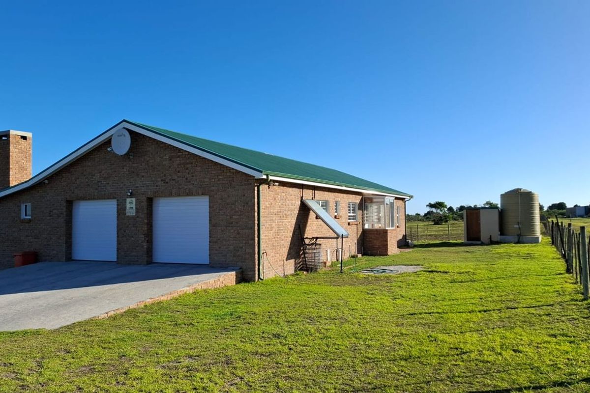 Rear view of a brick farmhouse featuring a double garage, metal roof, external chimney, solar water heating system, and a large water storage tank.