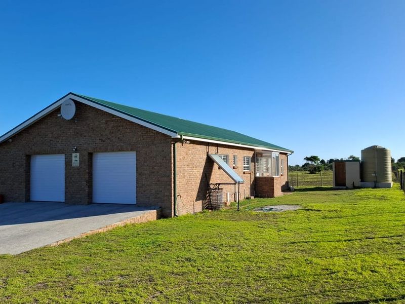 Rear view of a brick farmhouse featuring a double garage, metal roof, external chimney, solar water heating system, and a large water storage tank.