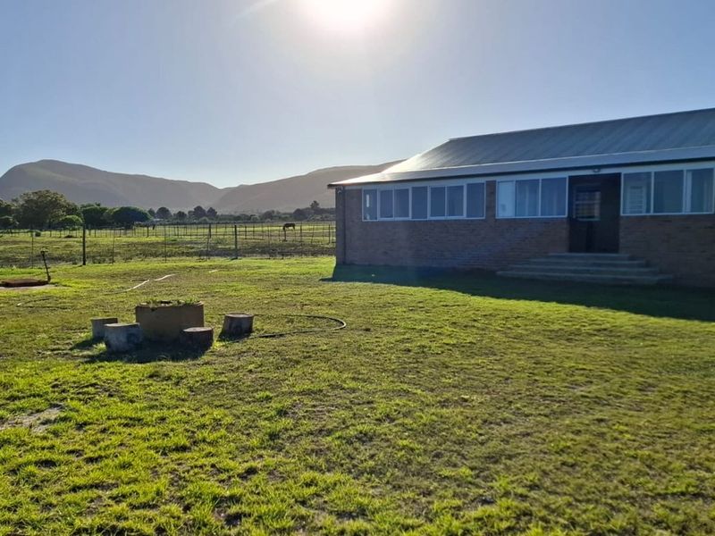 A rear view of a brick farmhouse featuring a metal roof and large windows, set against a scenic mountain landscape.