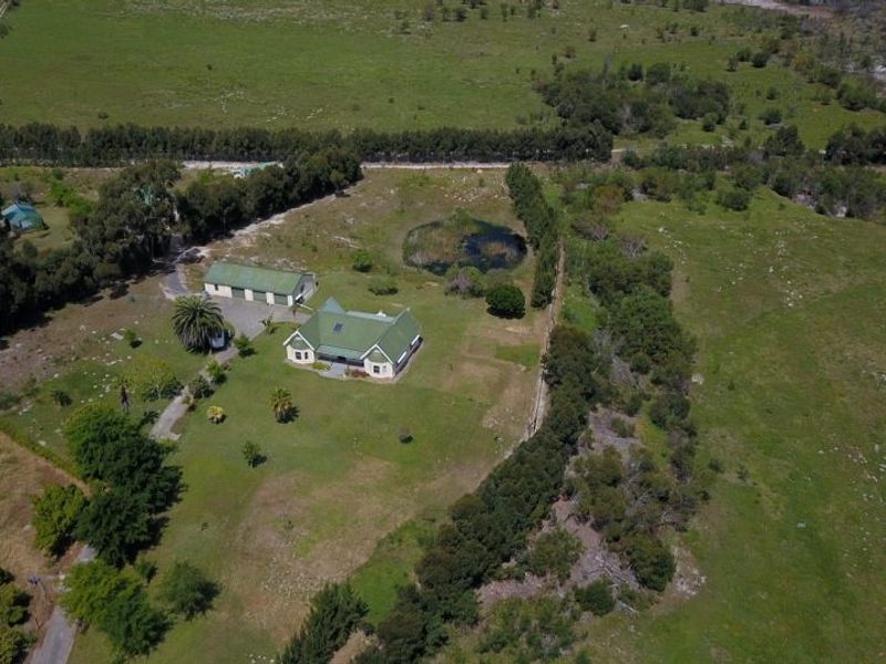 Aerial view of a farm property featuring a main residence with a green metal roof, a detached garage, and a small dam on the grounds.