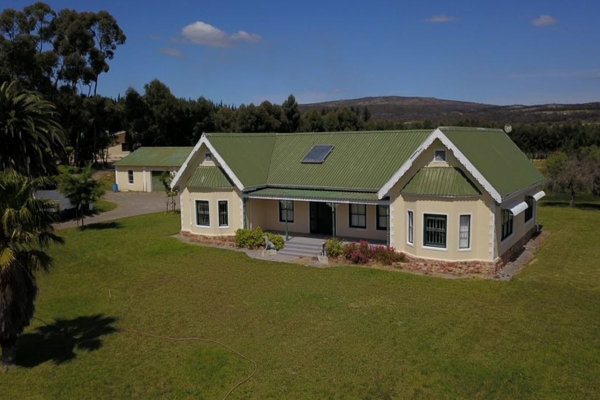 Aerial view of a well-maintained farmhouse featuring a green corrugated metal roof, solar water heating, and a spacious surrounding garden with a detached garage.