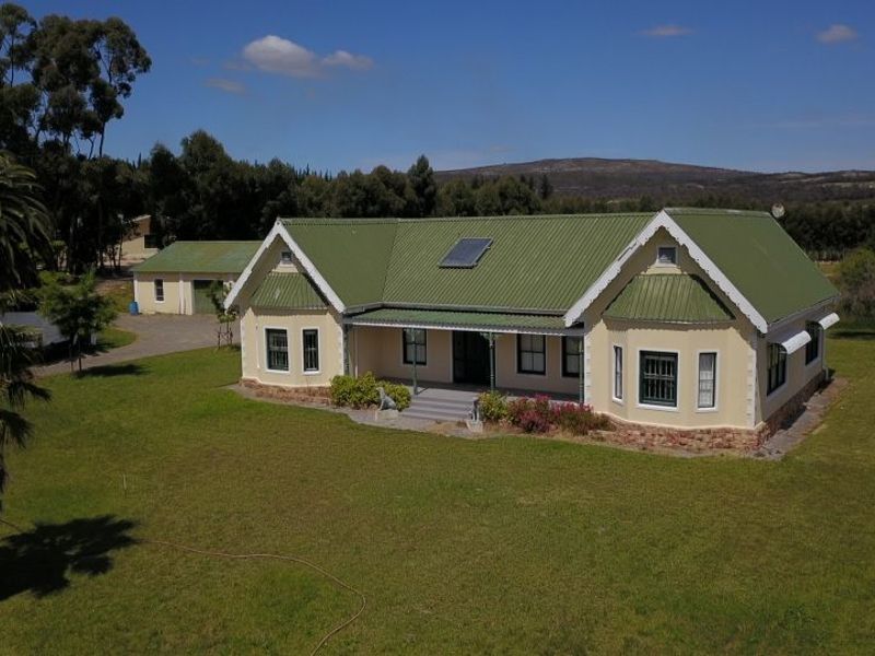 Aerial view of a well-maintained farmhouse featuring a green corrugated metal roof, solar water heating, and a spacious surrounding garden with a detached garage.