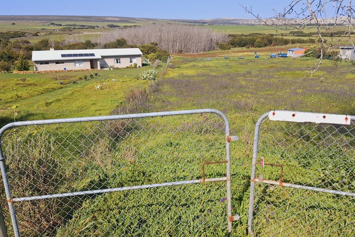 A wide-angle view of an agricultural property featuring a residential dwelling with solar panels, surrounded by open fields and secured by a wire fence.