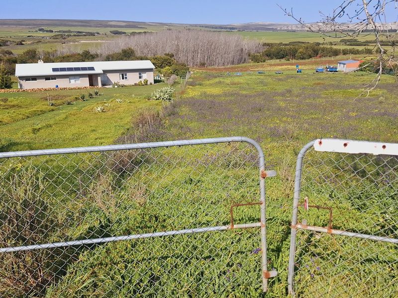 A wide-angle view of an agricultural property featuring a residential dwelling with solar panels, surrounded by open fields and secured by a wire fence.