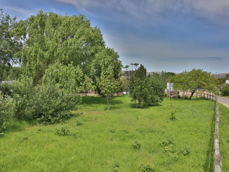 A view of a vacant residential plot featuring established trees, a grass lawn, and a wooden post and rail boundary fence.