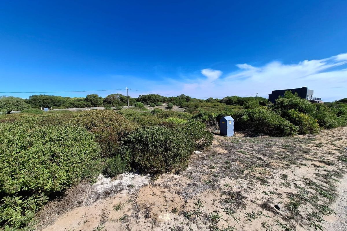 A vacant commercial land plot featuring native coastal vegetation, sandy terrain, and an existing electrical utility connection point.