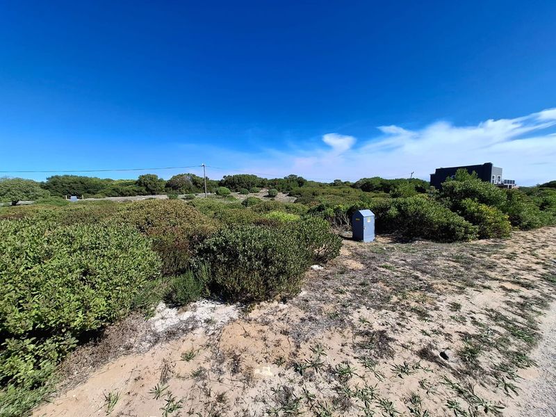 A vacant commercial land plot featuring native coastal vegetation, sandy terrain, and an existing electrical utility connection point.