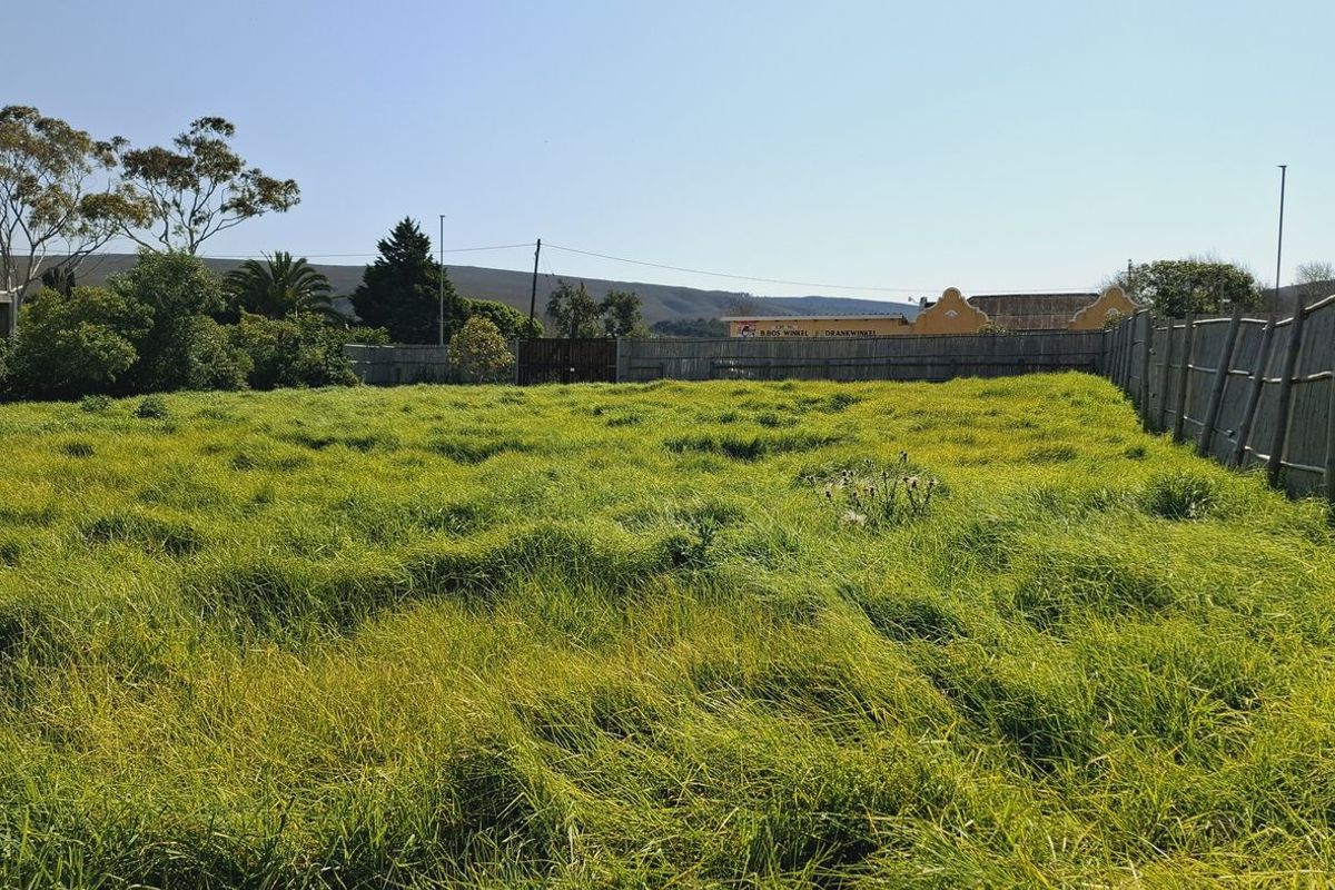 A vacant residential plot featuring established grass coverage and perimeter timber pole fencing, offering a clear space for future development.