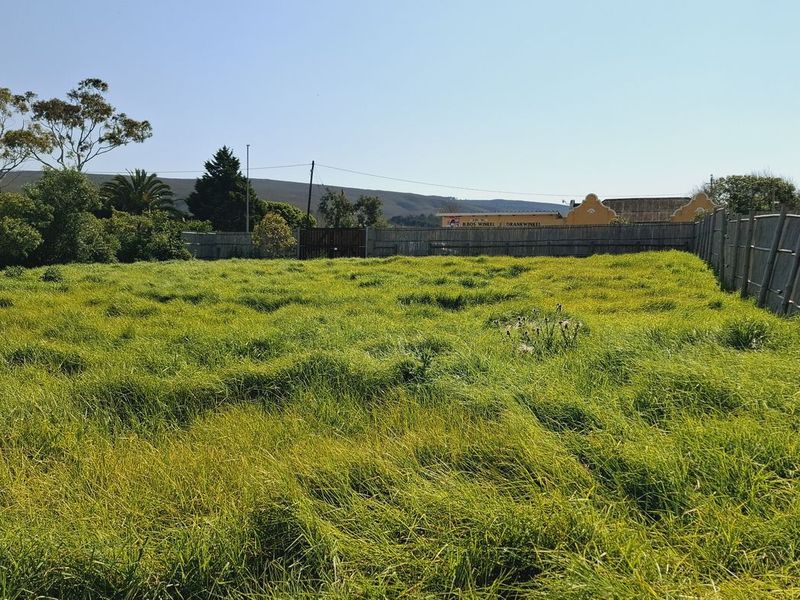 A vacant residential plot featuring established grass coverage and perimeter timber pole fencing, offering a clear space for future development.