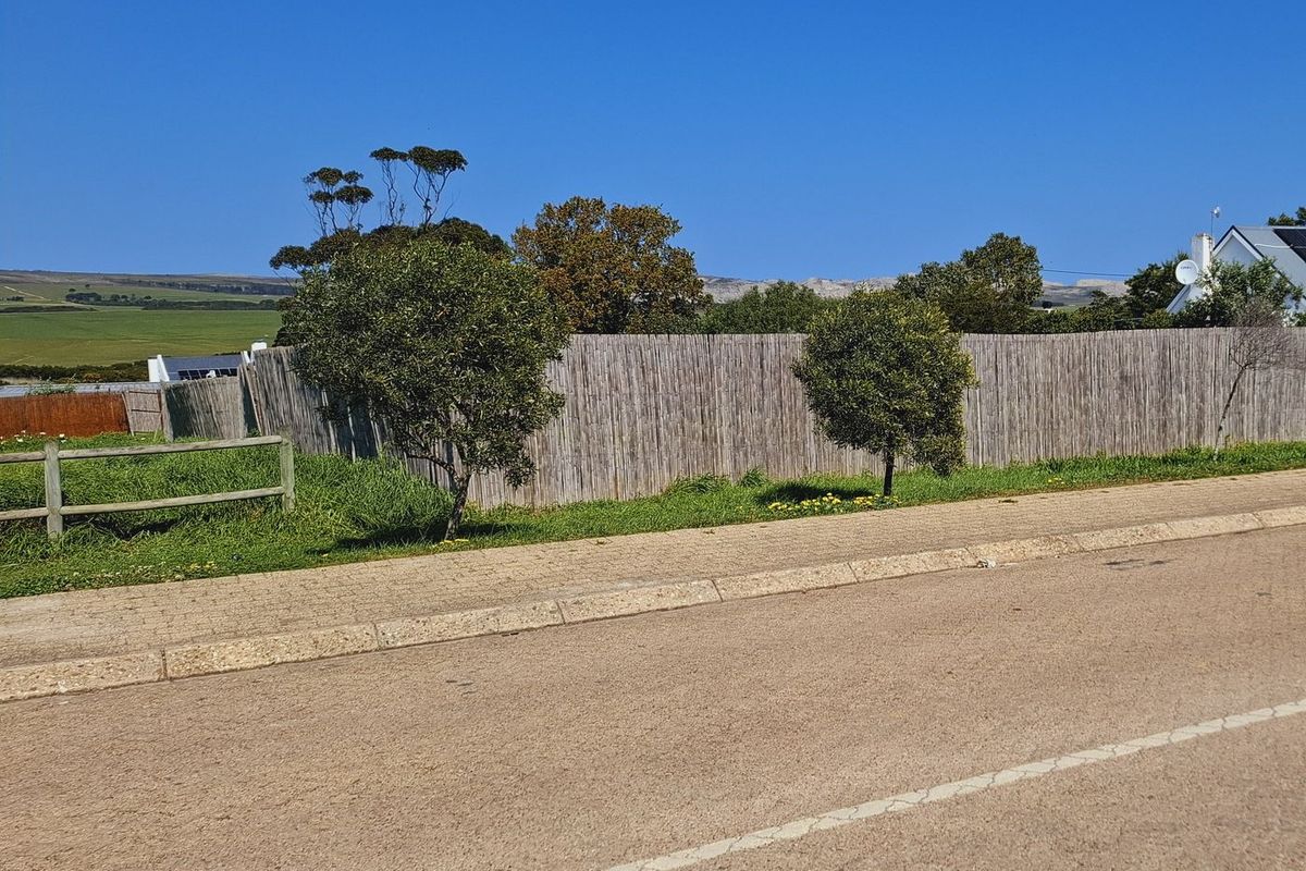 Street view of a residential vacant land plot featuring established reed fencing, timber boundary fencing, and a paved curb.