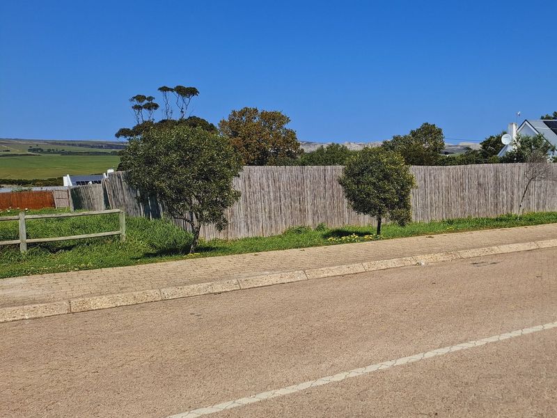 Street view of a residential vacant land plot featuring established reed fencing, timber boundary fencing, and a paved curb.