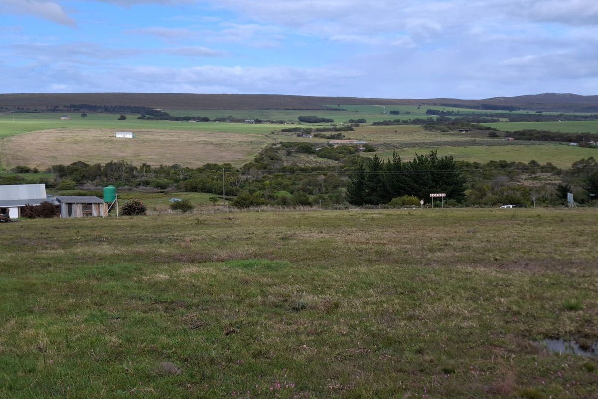 Expansive rural landscape view featuring open grazing land, distant hills, and a small outbuilding with a water tank.