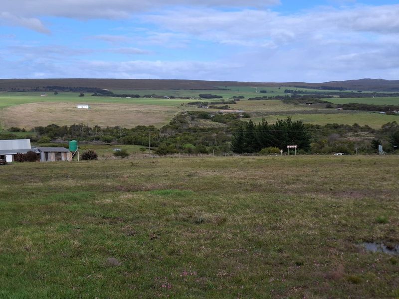 Expansive rural landscape view featuring open grazing land, distant hills, and a small outbuilding with a water tank.