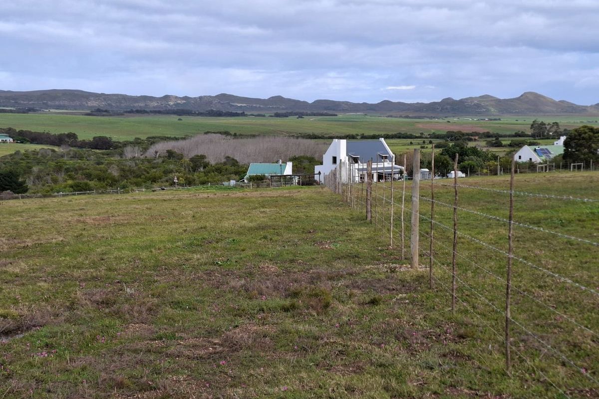 Expansive rural landscape view featuring rolling hills and distant mountains, framed by a traditional barbed wire farm fence.