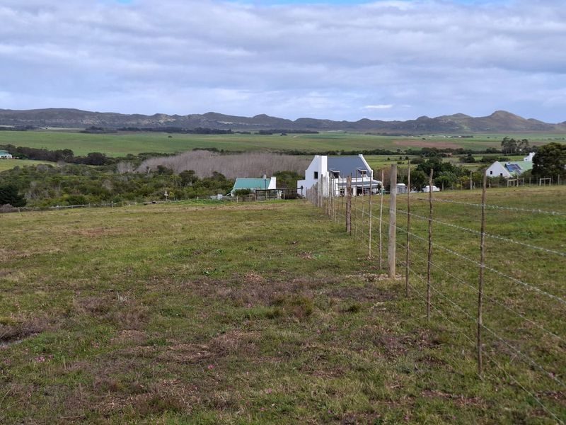 Expansive rural landscape view featuring rolling hills and distant mountains, framed by a traditional barbed wire farm fence.