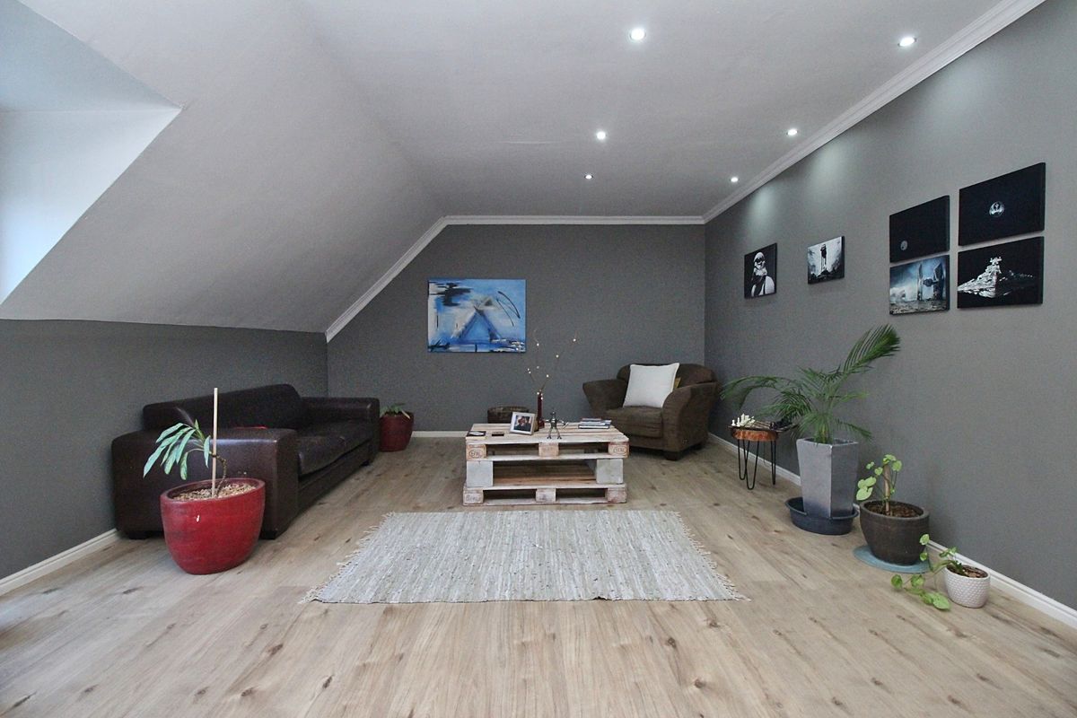 A spacious living room featuring modern grey walls, recessed ceiling lighting, and light wood-look flooring under a sloped ceiling.