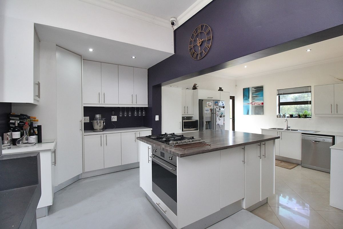 Modern open-plan kitchen featuring a central island with a built-in oven and gas hob, complemented by sleek white cabinetry and dark accent walls.