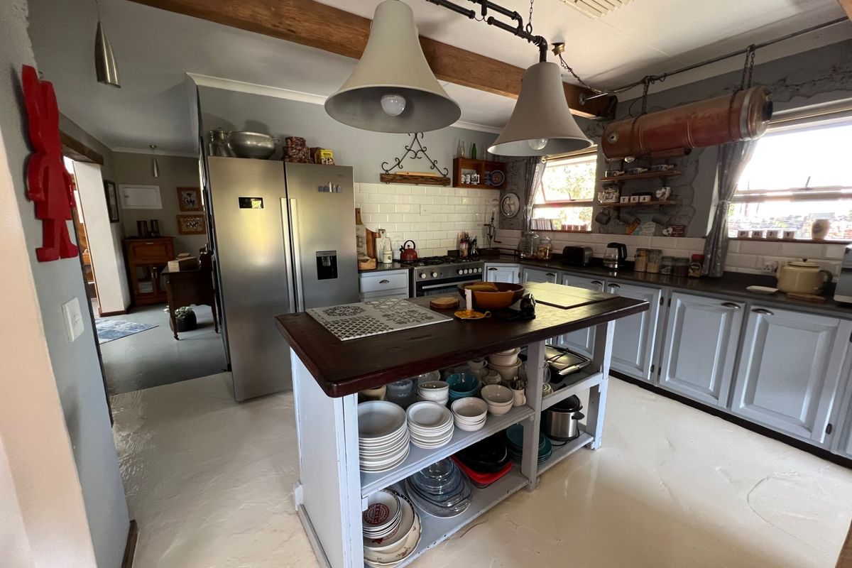 A rustic-style kitchen featuring a central island, subway tile backsplash, exposed wooden ceiling beams, and industrial-style pendant lighting.