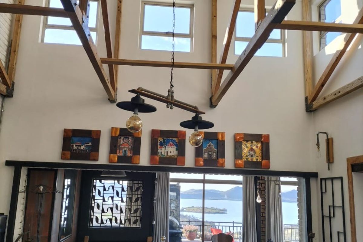Spacious living area featuring high vaulted ceilings with exposed timber trusses, large windows, and direct access to a balcony with scenic water views.