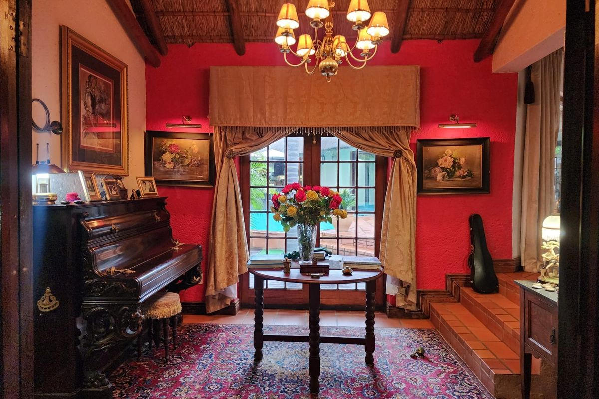 A cozy living room featuring a vaulted thatched ceiling, terracotta tiled flooring, and French doors opening to a pool area.