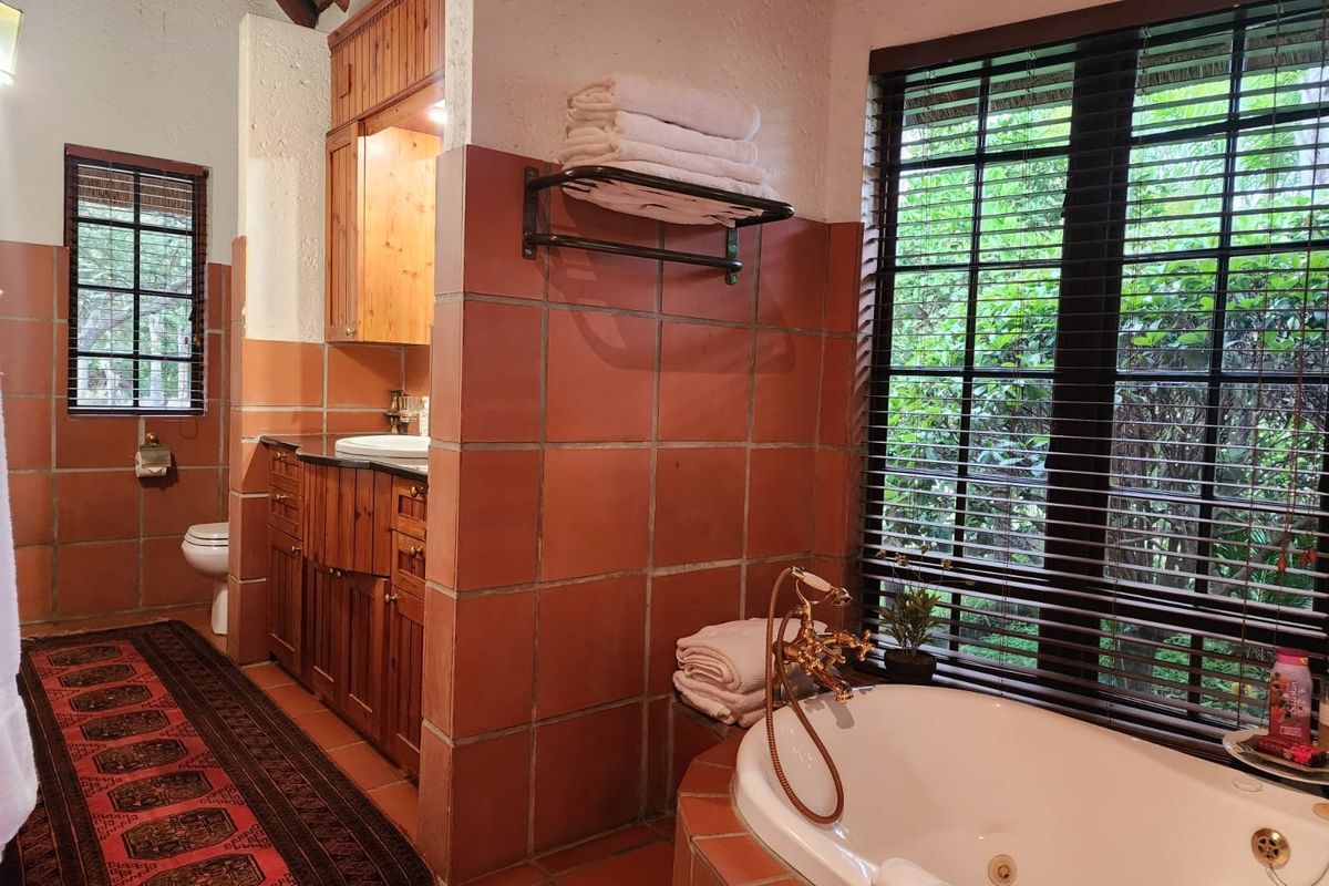 A rustic-style bathroom featuring a built-in bathtub with brass fixtures, terracotta floor and wall tiles, and wooden cabinetry with a vanity basin.