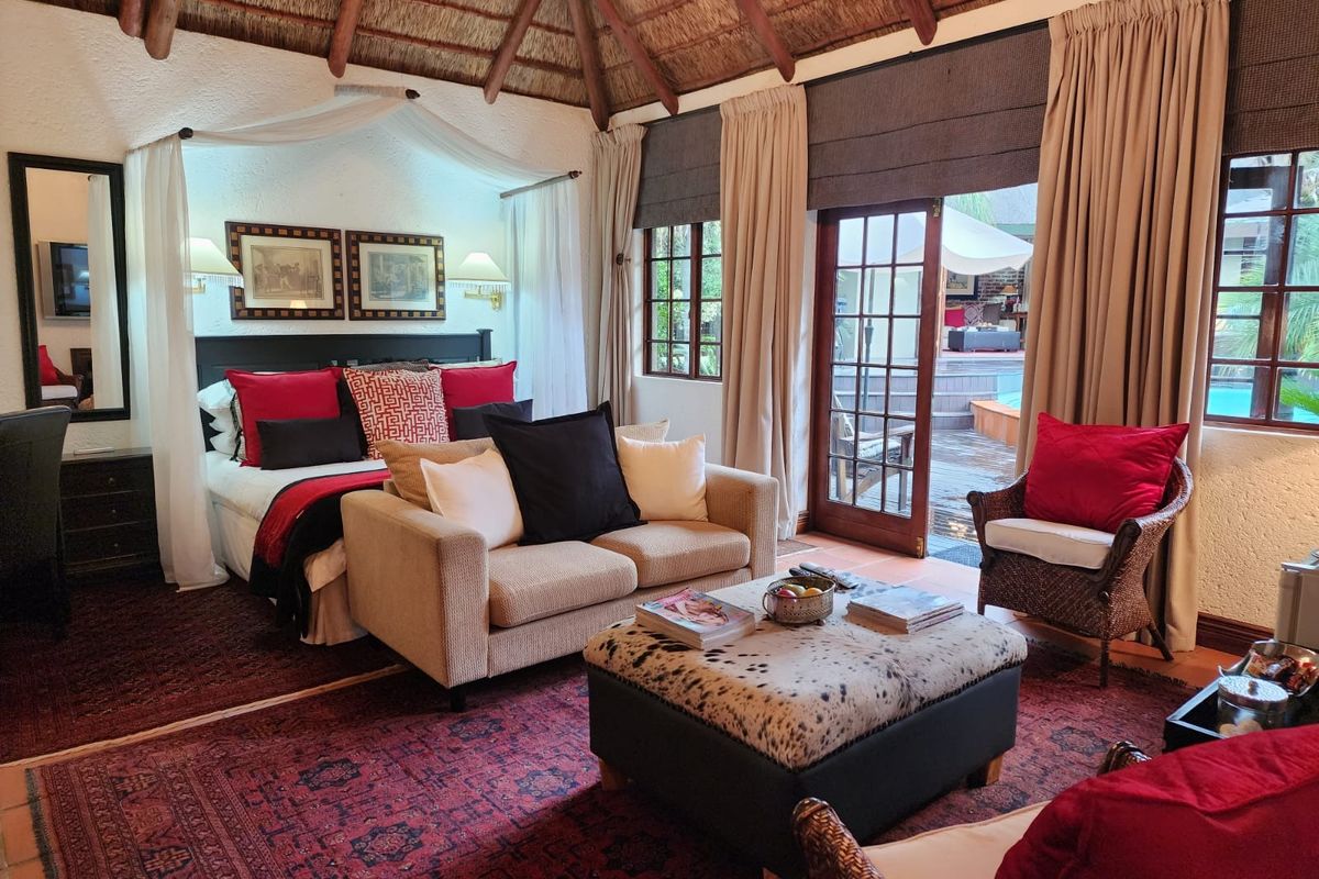 Spacious bedroom featuring a high thatched ceiling, exposed timber beams, and direct access to an outdoor patio area through glass-paned doors.